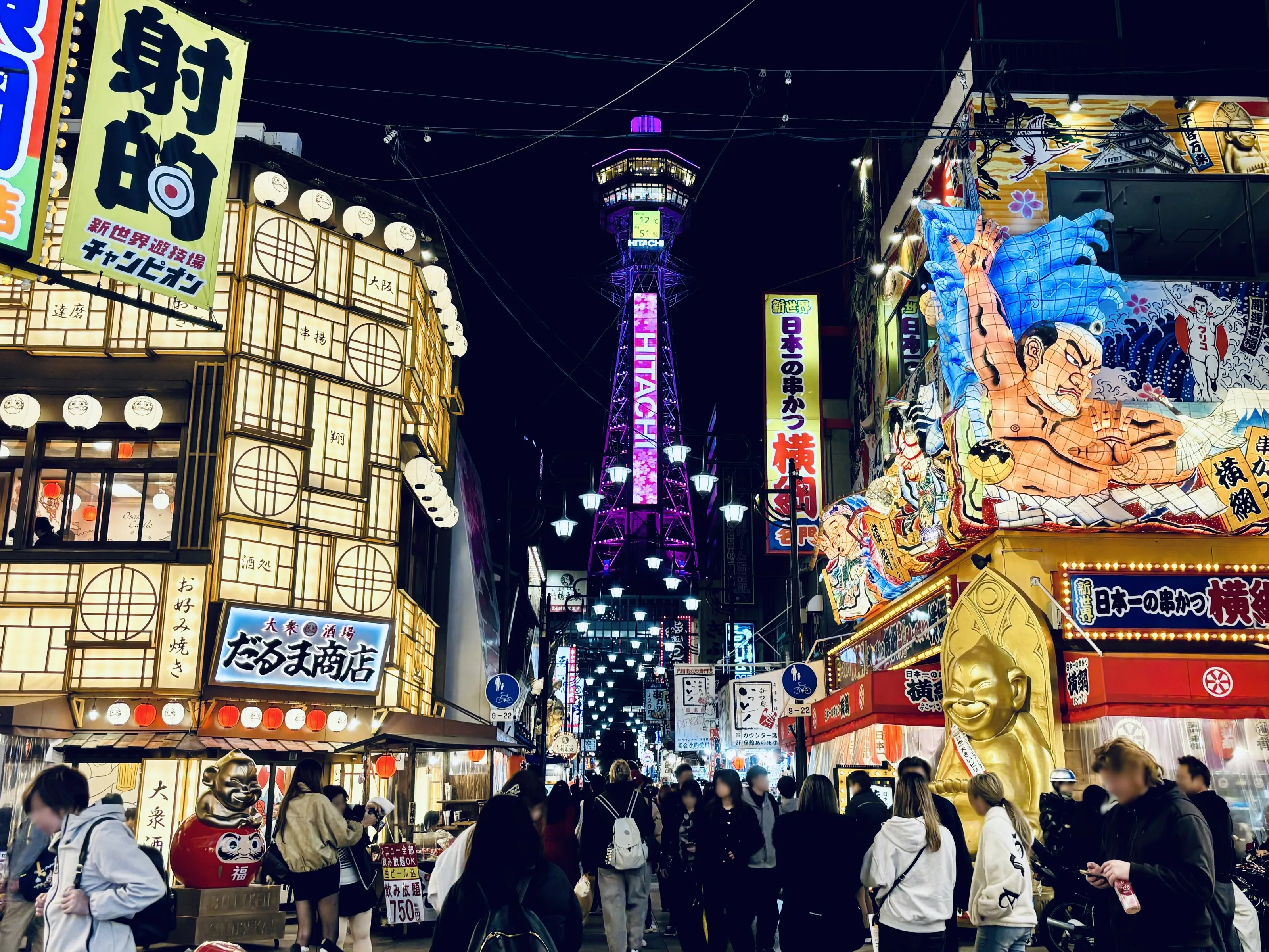 Neon signs and crowds under Tsutenkaku Tower in Shinsekai at night