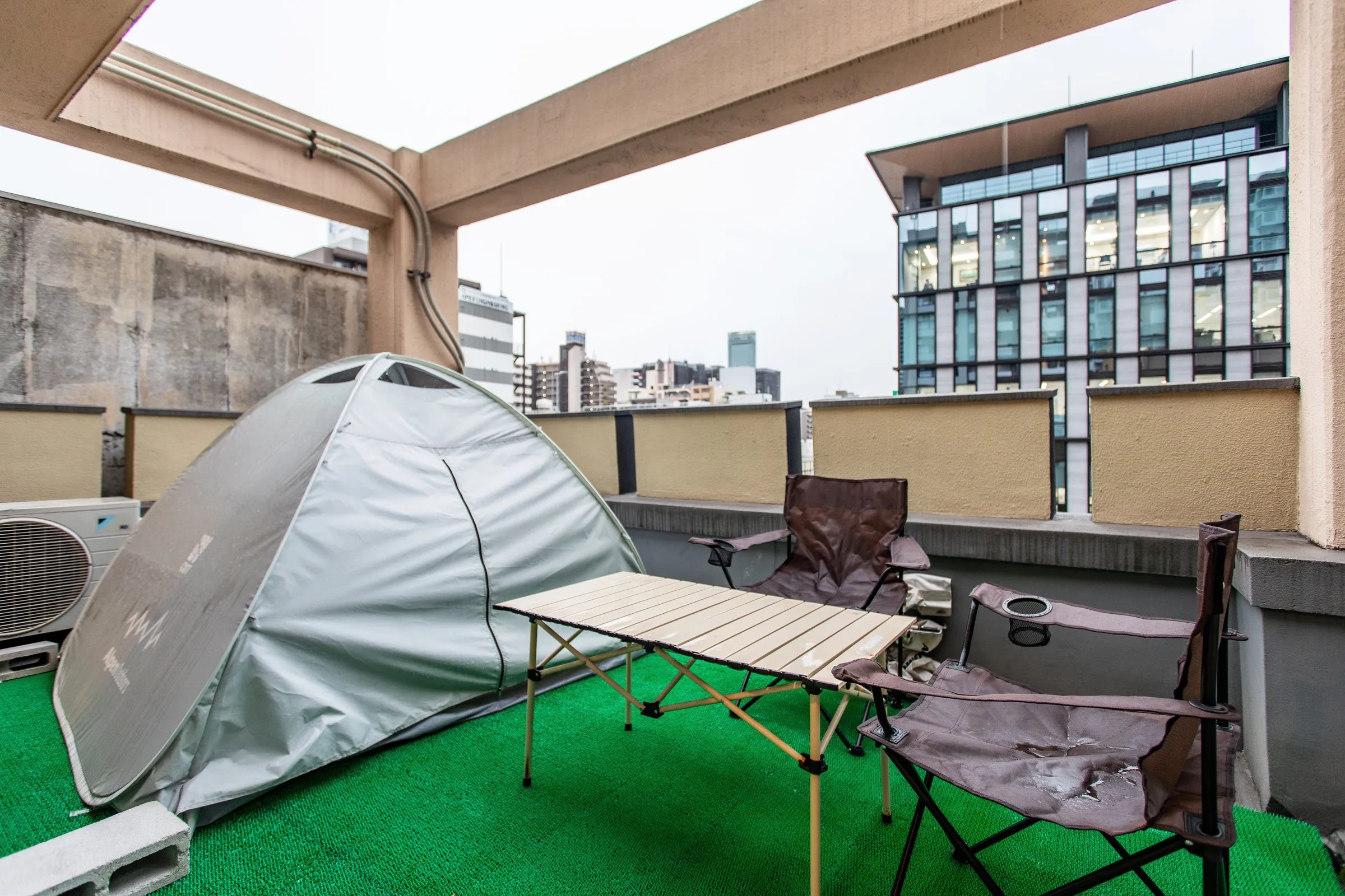 テントとキャンプチェアのある屋上テラス、背景に街の夜景